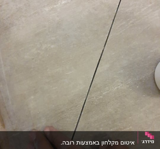 יד נוגעת ברווח בין אריחים על רצפה